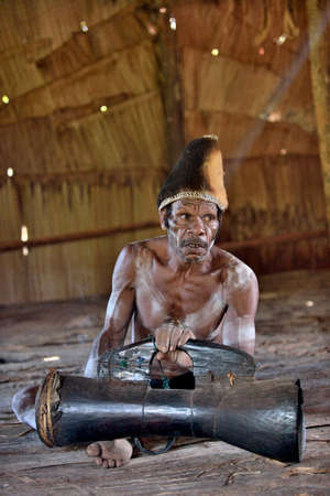 YOUW VILLAGE, ATSY DISTRICT, ASMAT REGION, IRIAN JAYA, NEW GUINEA, INDONESIA - MAY 23, 2016: Asmat with a drum. Man from the tribe of Asmat with traditional face painting beats the drum. May 23, 2016のeditorial素材