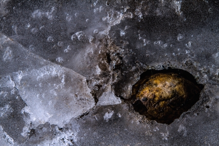 Frozen pond with cracks, bubbles, rocks and ice creating a network of textures and lines の写真素材