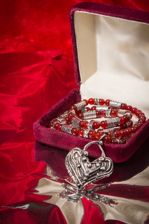 Silver and red stone necklace cascades from jewelry box on red velvet background の写真素材