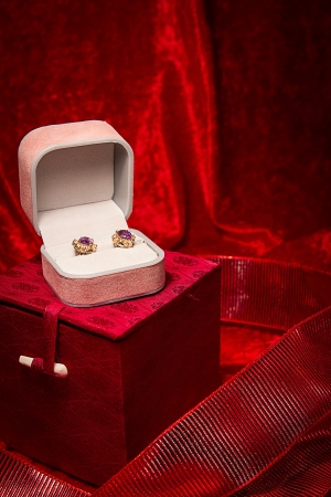 Pair of earrings rest in open jewelry box on red velvet backgound の写真素材