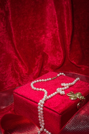Pearl necklace cascades from jewelry box on red velvet background.の写真素材