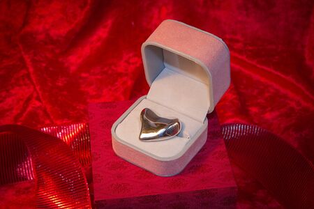 Silver heart rests in open jewelry box on red velvet backgound.の写真素材
