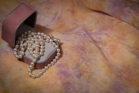 Pearl necklace cascades from jewelry box on pink and yellow pastel background.の写真素材