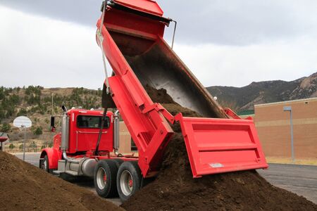 Big red dump truck dumps pile of dirt.のeditorial素材