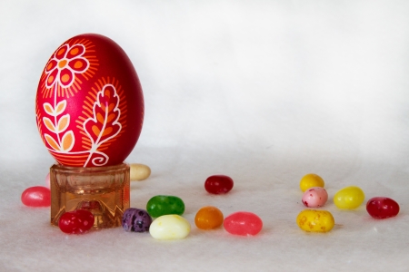 A decorated red Easter egg stands next to jelly beans on a white background in horizontal...