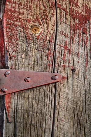 Weathered barn wood shows worn red paint and knots in grain plus  antique hings with bolts.の写真素材