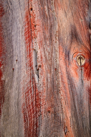 Weathered barn wood shows worn red paint and knots in grain.の写真素材