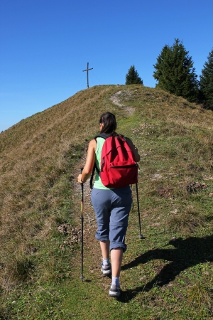 Mountaineering woman walking towards mountain cross, bavarian landscapeの写真素材