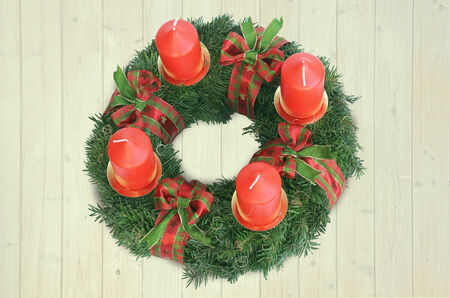 homemade advent wreath on light wooden background, with red candles and red and green patterned ribbonの写真素材