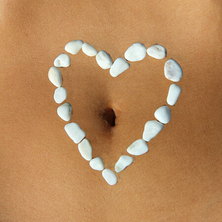 Womans belly closeup with heart made of white pebble stones around the belly bottomの写真素材