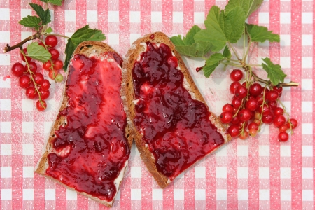 Bread slices with red current jam on nostalgic red and white checkered slat, rustic breakfastの写真素材