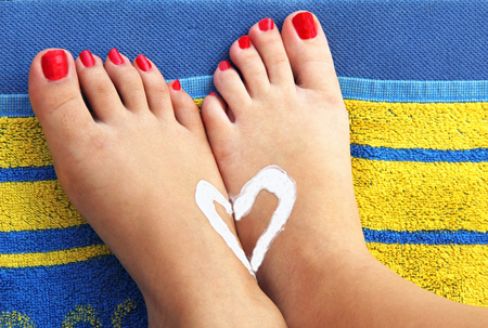 Teenage girls feet on an beach towel with sunlotion heart, summer holidaysの写真素材