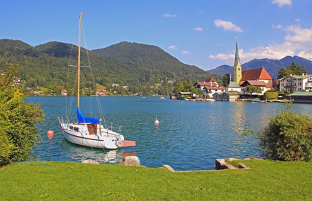 Beautiful cove of lake tegernsee with sailboat and rottach-egern village, germanyの写真素材