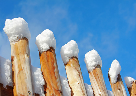 wooden fence with snow caps, blue skyの写真素材