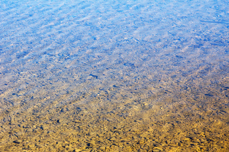 shallow water with stony ground, blue sky reflectionの写真素材