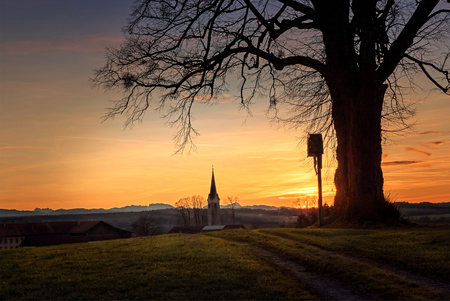 hill with tree and wayside cross, dreamy sunset scenery with view to village and alps, upper bavariaの写真素材