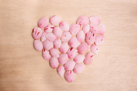 pink floral heart made of camellia flower petals on wooden background