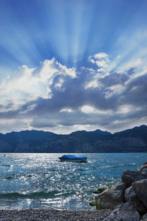 beautiful garda lake with little boat. dramatic cloud with sunbeams, italyの写真素材