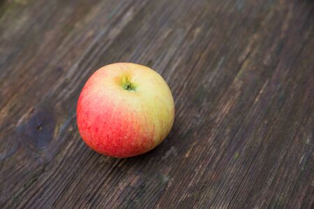 one apple red and yellow on a rustic dark brown wooden table, narrow depth of field and space for textの写真素材