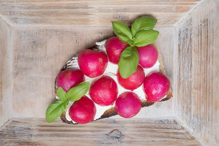 Slice of bread spread with cream cheese and topped with half radishes, vintage wooden backgroundの写真素材