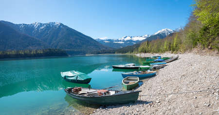 moored fishing boats at lake shore Sylvensteinsee, bavarian landscape at springtimeの写真素材