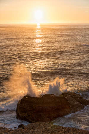 rock in the surf at sunset, romantic seascape with sinking sun. coastal landscape portugalの写真素材
