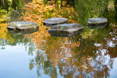 four big stones in a pond, autumnal trees reflecting in the water. seasonal backgroundの写真素材