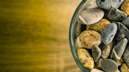 Small sea stones in a glass vessel. The idea of decorating the house with small rocks in a jar on a wooden blurred background.の写真素材