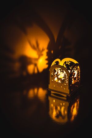Christmas decoration on a shiny surface. A small wooden lantern with a candle inside casting a shadow on a golden background.の写真素材