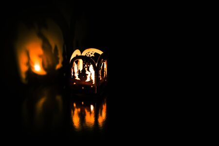A small wooden lantern with a candle inside casting a shadow on a golden background.の写真素材