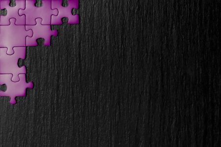 Purple puzzle in the corner of the image on a black natural stone background of slate. A frame with an empty space for your description.の写真素材