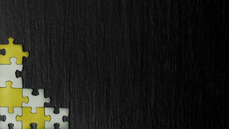 Silver and golden puzzle in the corner of the image on a black natural stone background of slate. A frame with an empty space for your description.の写真素材