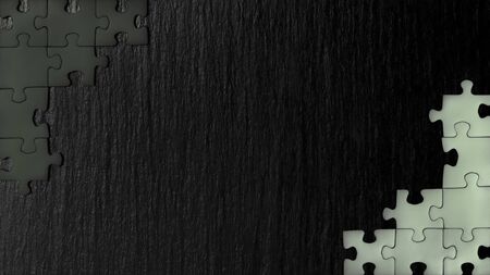 Black nd white puzzle in the corner of the image on a black natural stone background of slate. A frame with an empty space for your description.の写真素材