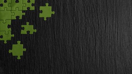 Green puzzle in the corner of the image on a black natural stone background of slate. A frame with an empty space for your description.の写真素材