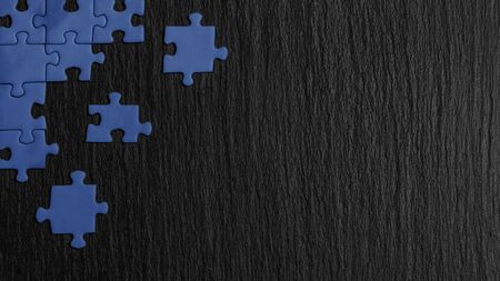Blue puzzle in the corner of the image on a black natural stone background of slate. A frame with an empty space for your description.の写真素材