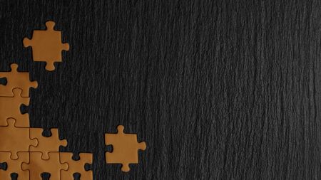Orange puzzle in the corner of the image on a black natural stone background of slate. A frame with an empty space for your description.の写真素材