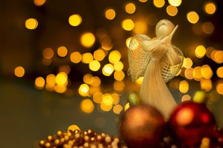 Traditional hand made straw doll with Christmas ornaments on a blurred background with lights. Dramatic Christmas landscape with dried straw angel who prays. A christmas tree decoration.の写真素材