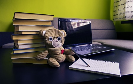 Close up of teddy bear writing down some notes. Notebook and books in the background.の写真素材