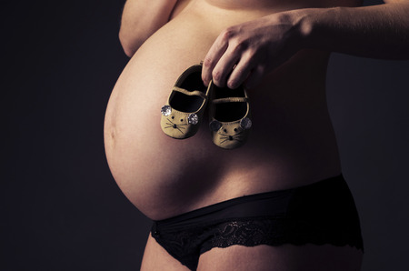 Close up of baby shoes and pregnant woman