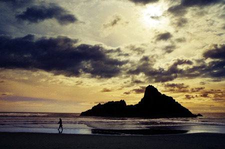 Amazing view of sunset on the beach. Woman walking on the beach. Rocks in the background.の写真素材