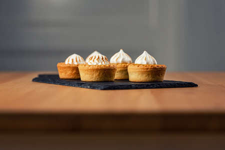 Close up of mini tartalets on a slate chopping board. Small tartalets with orange curd and meringue on the top. Sweet desserts. Sweet catering.の写真素材