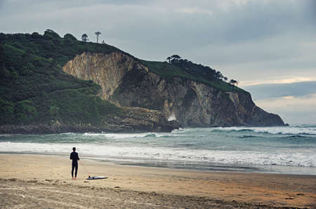 Surfing concept. Love surfing. Surfer standing on the beach and looking at waves in the ocean....