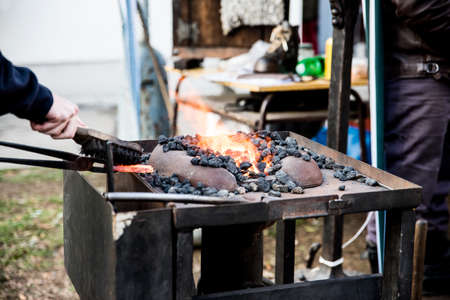 Close up of hands working with iron in an open fire. A blacksmith works with iron.