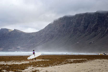 Female surfer, beach and hills in the background. Surfing at begginer level.の写真素材
