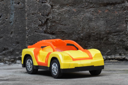 Yellow toy car on cement floor with brick wall in the background.