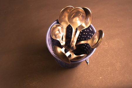 Metal spoons in a blue basket on a brown surface.の写真素材