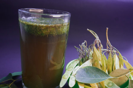 A glass of green tea with fresh leaves and flowers on a purple background