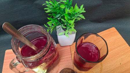 Cup of red juice on wooden board with green plant on black background