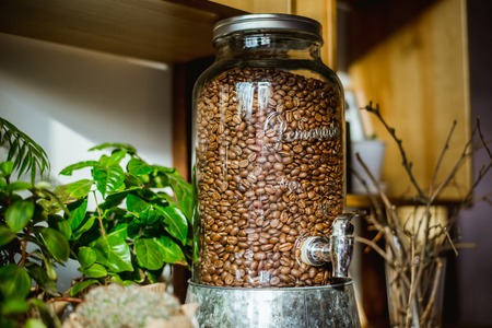 Glass container of coffee beans is on the tableの写真素材