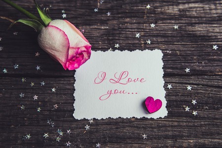 Pink roses with a note declarations of love. On a wooden boardの写真素材